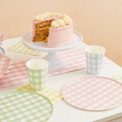 Bolo decorado numa base branca com copos e pratos quadriculados em várias cores