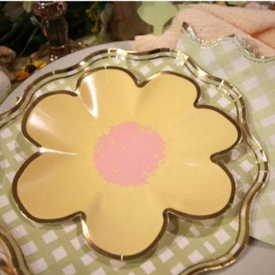 Prato decorativo amarelo em forma de flor sobre tecido xadrez verde e branco