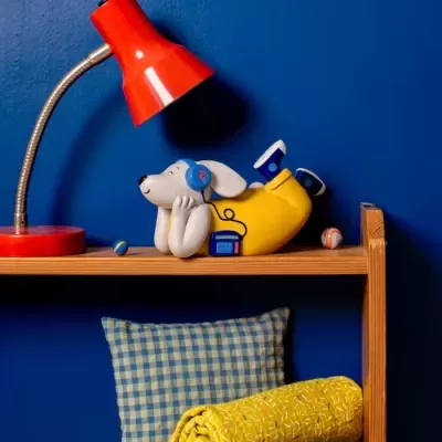 Estante de madeira com candeeiro vermelho e decoração, incluindo figura de cão com auscultadores e rádio.