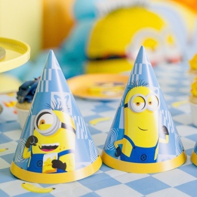 Chapéus de festa de papel dos Minions em padrão azul e amarelo sobre uma mesa decorada.