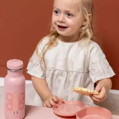 Criança segurando biscoito junto a garrafa e recipientes rosas sobre mesa rosa
