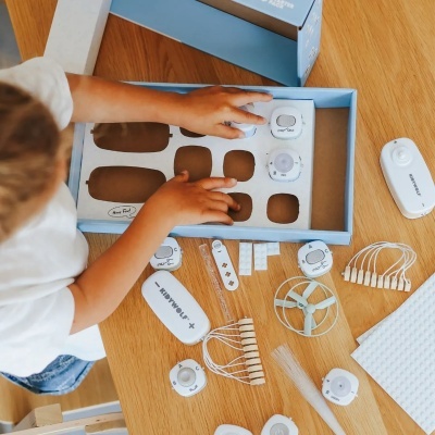 Kit educativo de peças eletrónicas brancas e cinza sobre uma mesa de madeira com um estojo azul