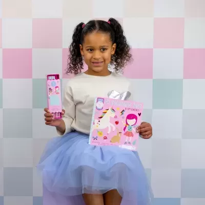 Menina segurando um livro de colorir e lápis de cor em fundo quadriculado pastel