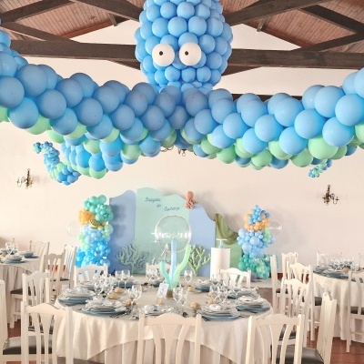 Sala com mesas decoradas para batizado com balões azuis e verdes em forma de polvo