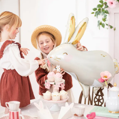 Balão de coelho prateado com crianças e mesa decorada com doces e flores