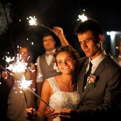Casal vestido formal segurando velas de fogo-de-artifício numa celebração noturna