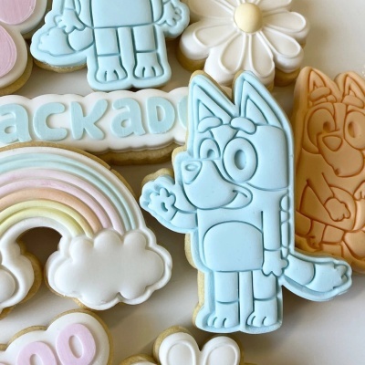 Biscoitos decorados com glacê em várias formas e cores pastel, incluindo personagem azul e arco-íris.