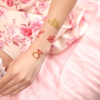 Braço com tatuagens temporárias douradas e vermelhas, vestido rosa floral