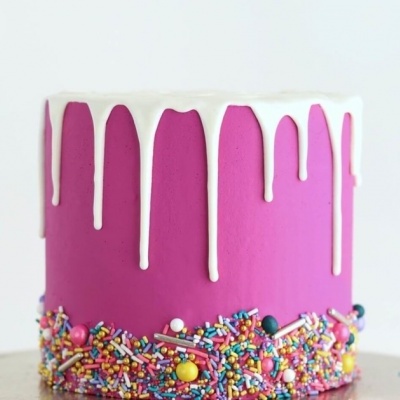 Bolo rosa com cobertura branca a escorrer e granulados coloridos na base