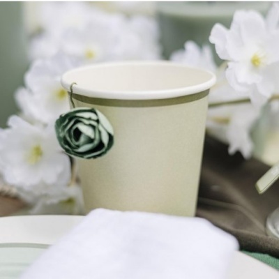 Copo descartável bege com uma alça de chá em forma de flor verde ao fundo flores brancas