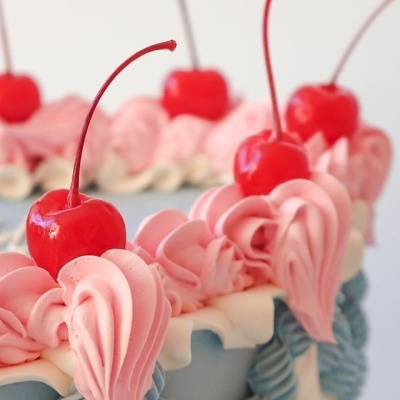 Bolo decorado com chantilly rosa e branco e cerejas vermelhas no topo.