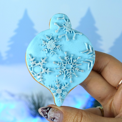 Biscoito azul decorado com flocos de neve segurado por mão com unhas decoradas