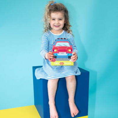 Criança sorridente com vestido às riscas segurando puzzle de carro colorido sentada em caixa azul