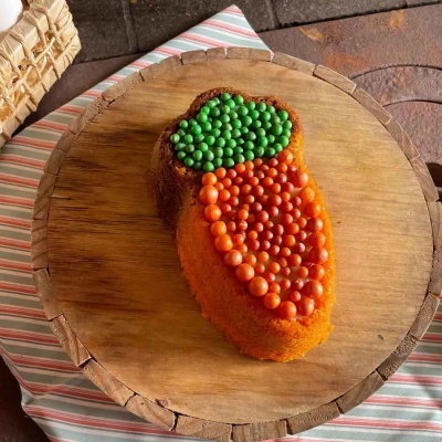Bolo em forma de cenoura decorado com bolinhas verdes e laranja numa base de madeira redonda