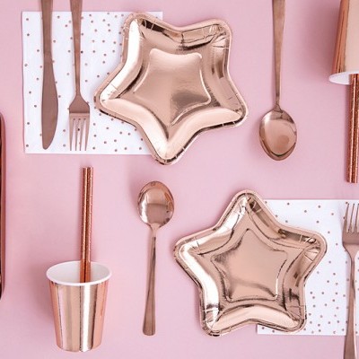 Mesa decorada para festa com pratos estrela rosa metálico, talheres rosa, copos com riscas rosa, guardanapos brancos com pontos dourados e caixa de macarons coloridos.