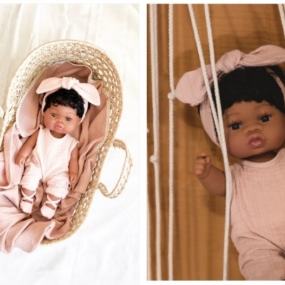 Boneca negra vestida de rosa bebé em carrinho de palha e suspensa em suporte de tecido branco