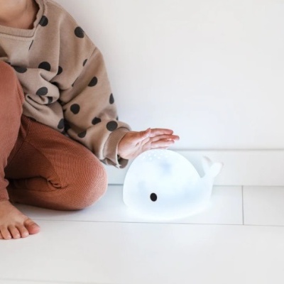 Criança sentada ao lado de brinquedo de baleia azul clara no chão branco