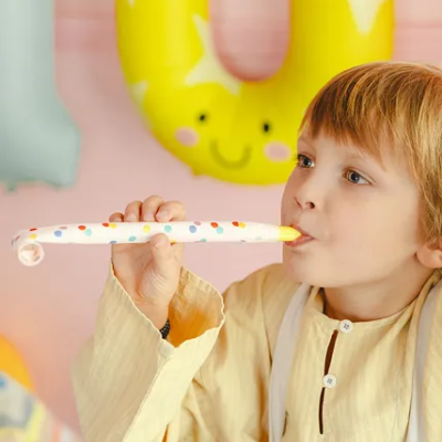 Criança loira com tosquiador de festa branco com pontos coloridos, balões amarelos decorativos ao fundo