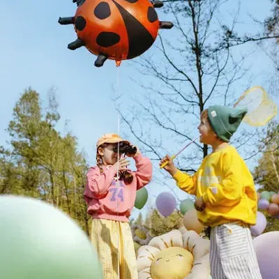 Duas crianças brincando ao ar livre com balões coloridos e balão de joaninha