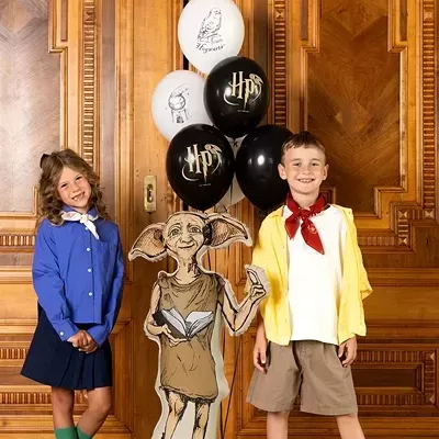 Crianças com roupas coloridas junto a balão inflável do personagem Dobby e balões temáticos preto e branco com texto HP