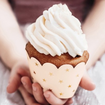 Cupcake com cobertura branca em embalagem com estrelas douradas segurado por duas mãos
