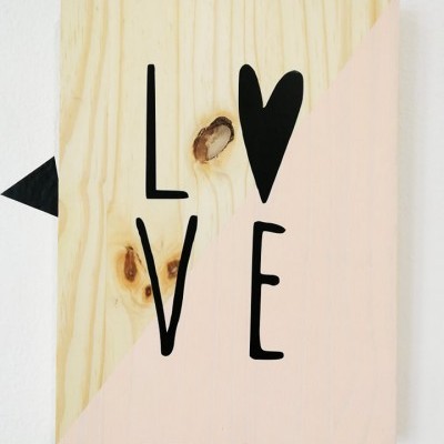 Placa de madeira decorativa com palavra LOVE e coração em preto sobre fundo natural e rosa claro