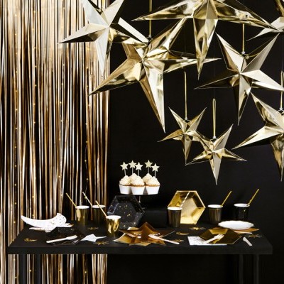 Decoração de festa em dourado e preto com estrelas, mesa com utensílios e cupcakes