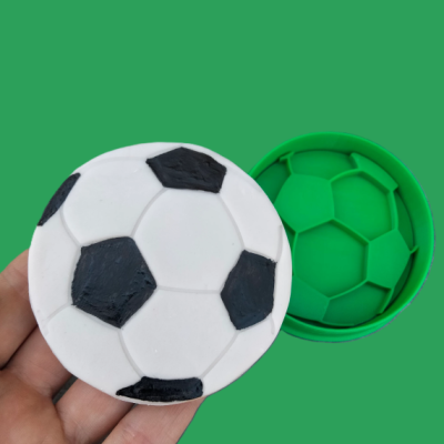 Caixa redonda verde com tampa e silicone branco e preto com padrão de bola de futebol
