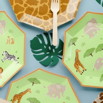 Pratos descartáveis com desenhos de animais da savana e garfos de madeira em fundo azul com folha decorativa verde