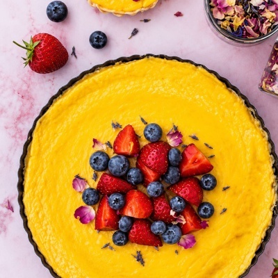 Tarte de creme amarelo decorada com morangos, mirtilos e flores secas