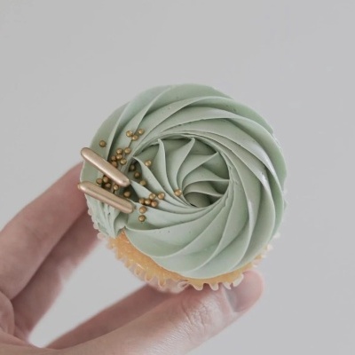 Cupcake com cobertura verde e decoração dourada numa mão