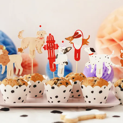 Bolinhos com toppers coloridos de cães e hidrante sobre prato branco em fundo festivo de bolas de papel