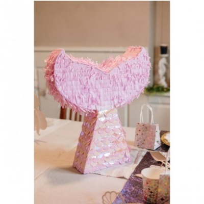 Piñata forma cauda de sereia rosa com franjas e escamas sobre mesa com copos e sacos de festa