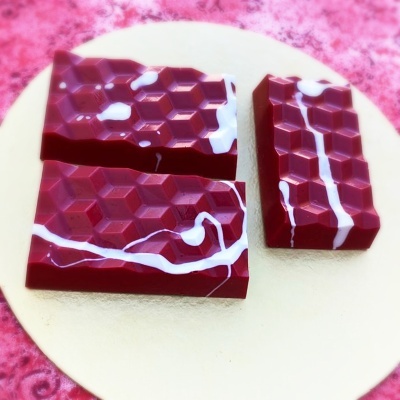 Barras de chocolate vermelho com padrão hexagonal e riscas brancas num prato dourado
