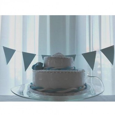 Bolo de dois andares branco com decoração azul e bandeirolas azuis ao fundo