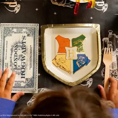 Conjunto de festa Harry Potter com prato de papel e convite do Mundo de Hogwarts sobre mesa preta com desenhos brancos