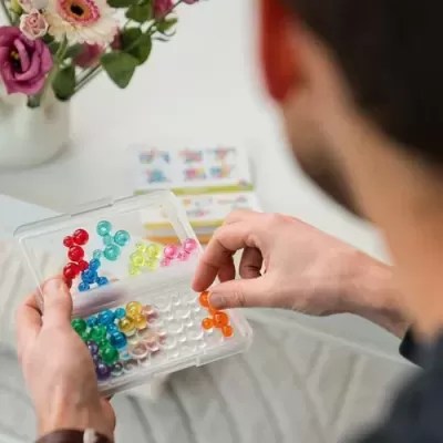 Pessoa a montar jogo de encaixe com esferas de plástico coloridas numa base transparente