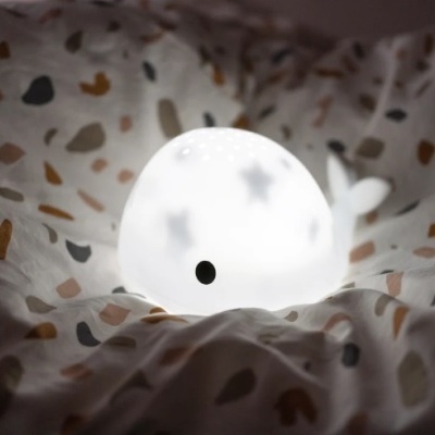 Luz noturna em forma de baleia branca com padrão de estrelas sobre tecido com manchas coloridas