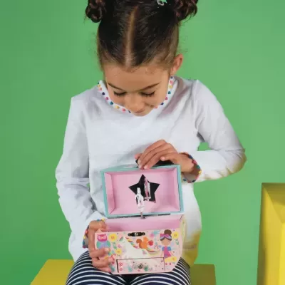 Criança com camisola branca segura caixa de música decorada em fundo verde