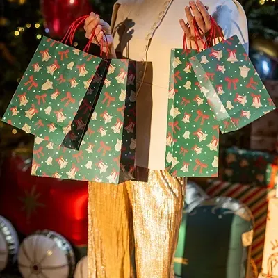 Mulher com sacos de presente verdes natalícios e roupa creme e dourada num cenário decorado para o Natal