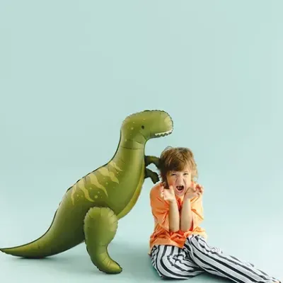 Criança sentada ao lado de balão de dinossauro verde