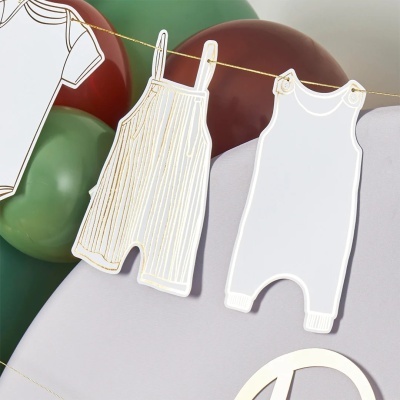 Cortes de papel em forma de roupa de bebê pendurados num varal com balões de fundo