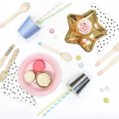 Talheres de madeira, guardanapos com padrões, pratos rosa e dourado, copo azul, doces coloridos e tubos decorativos