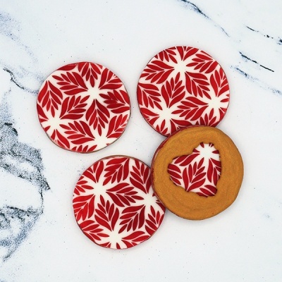 Biscoitos redondos com padrão vermelho e branco e biscoito dourado com recorte de coração sobre superfície branca