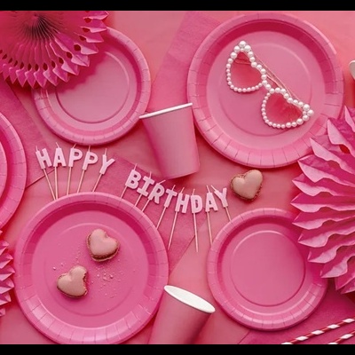Artigos para festa rosa com pratos, copos, decorações de papel, macarons, óculos e frase HAPPY BIRTHDAY.