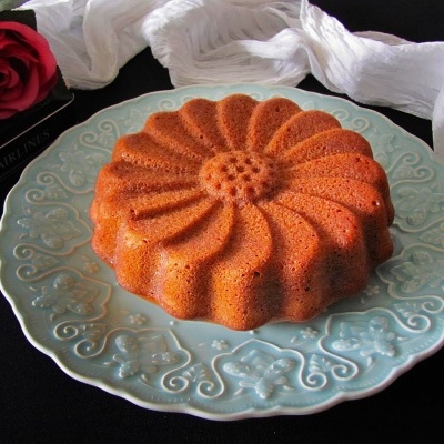 Bolo castanho em forma de flor num prato azul decorativo com lenço branco e rosa vermelha