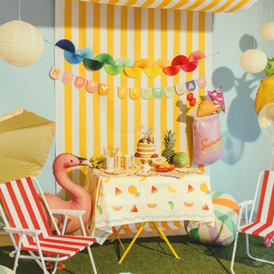 Mesa decorada para festa de aniversário com toalha com melancias, bolo, balões e cadeiras vermelhas e brancas de metal