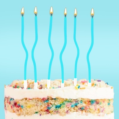 Bolo com glacê branco, granulados coloridos e cinco velas azuis acesas