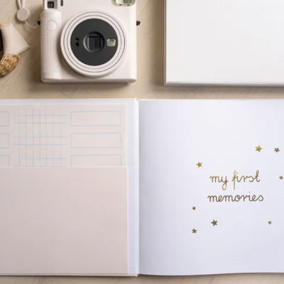 Álbum de memórias branco aberto com texto e estrelas douradas, câmara e itens de mesa