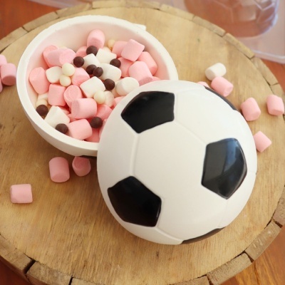 Tigela branca com tampa de bola de futebol cheia de mini marshmallows coloridos sobre madeira